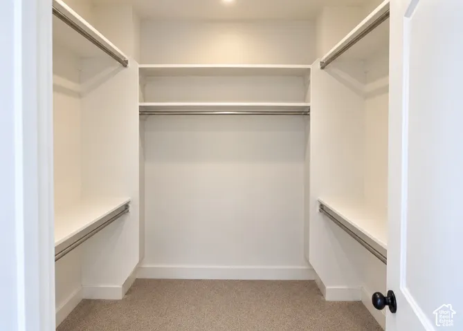 Large Primary Bedroom. Walk-in closet featuring white built-in shelving, dual-level metal hanging rods, and neutral carpeting