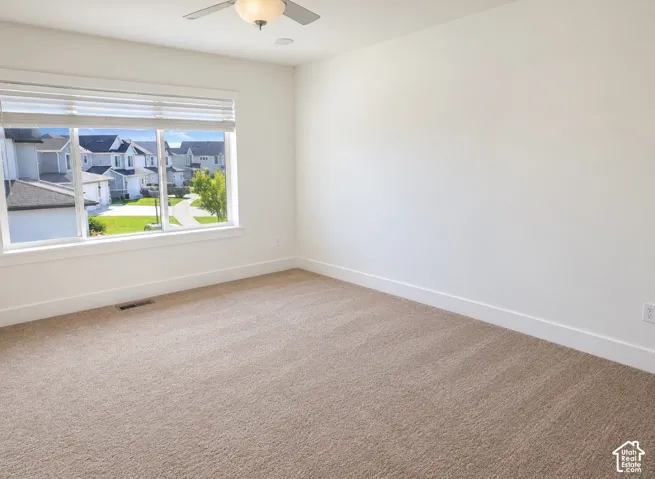Primary Bedroom. Neutral-toned carpeting, high-profile windows with integrated blinds, and a ceiling-mounted light fixture with a fan