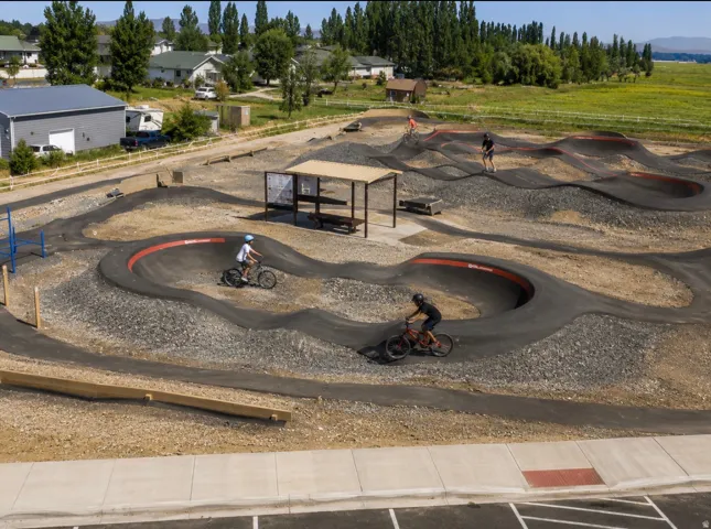 Pumptrack facility featuring asphalt tracks, gravel landscaping, and a shaded picnic area