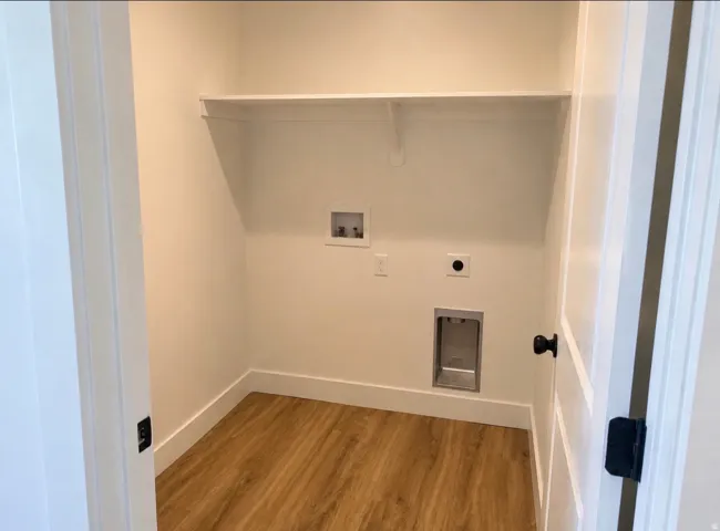 Utility area featuring wood-finish flooring, a wall-mounted shelf, and connections for laundry appliances