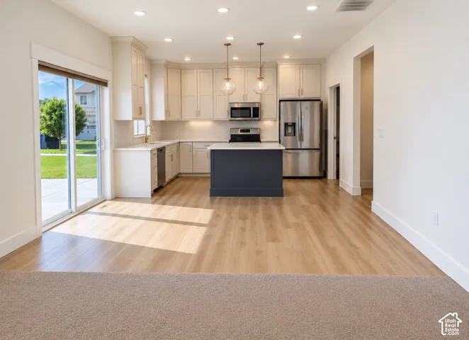 Kitchen featuring white shaker-style cabinetry, contrasting dark-toned central island, stainless steel appliances, recessed ceiling lighting, and sliding glass door