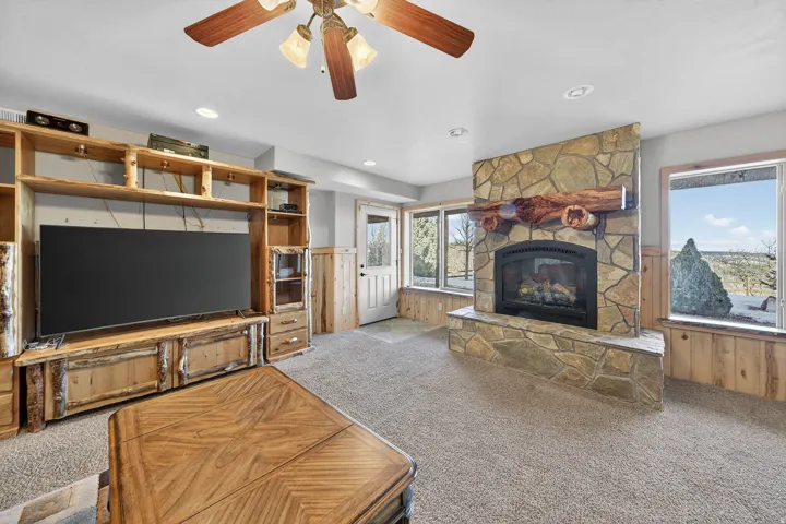 Stone-clad fireplace with a wood mantel, built-in wooden entertainment center, and ceiling fan with integrated lighting