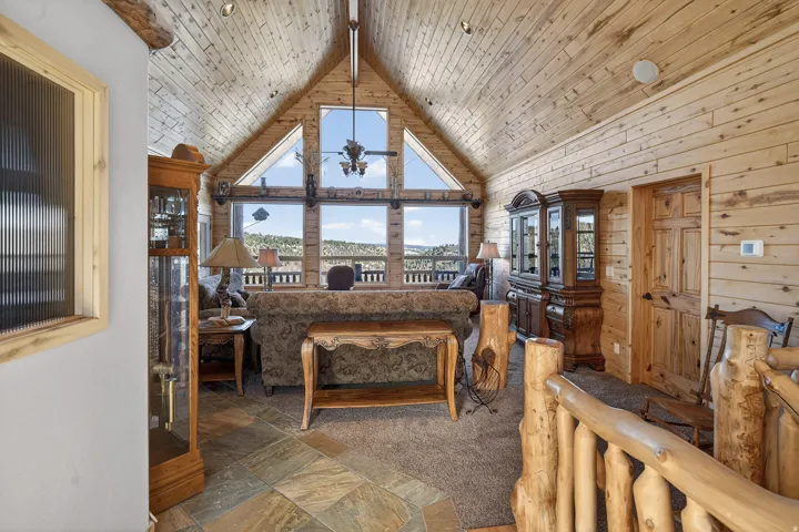 Vaulted wood-paneled ceiling, large picture windows, wood-finish flooring, wood-paneled walls, and a rustic wood railing
