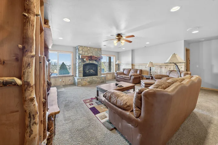 Stone-faced fireplace with a hearth, wood-paneled walls, multiple windows, recessed lighting, and a ceiling fan