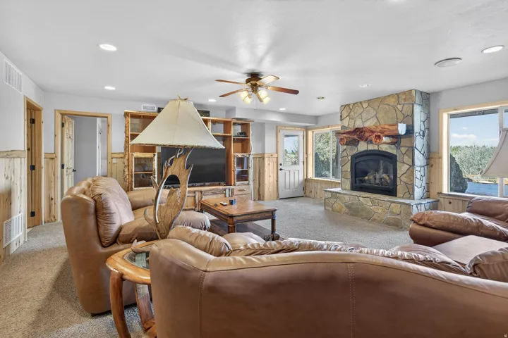 Carpeted living area featuring a stone-faced fireplace with a wood mantel, built-in shelving, recessed lighting, and a ceiling fan