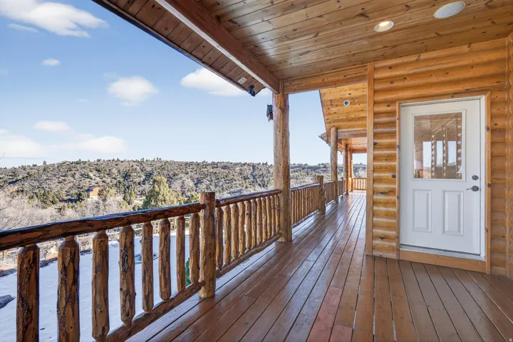 Expansive wood-finish deck with log railing, natural wood siding, wood-paneled ceiling, and recessed lighting