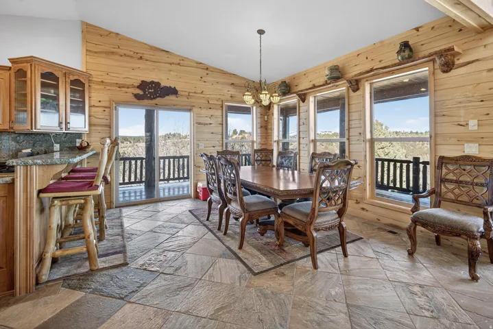Sloped ceiling with natural wood paneling, stone-tile flooring, multiple large windows, and a glass sliding door