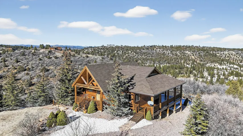 Log cabin exterior with an A-frame entrance, covered porch, and elevated deck, surrounded by mature trees and natural landscaping