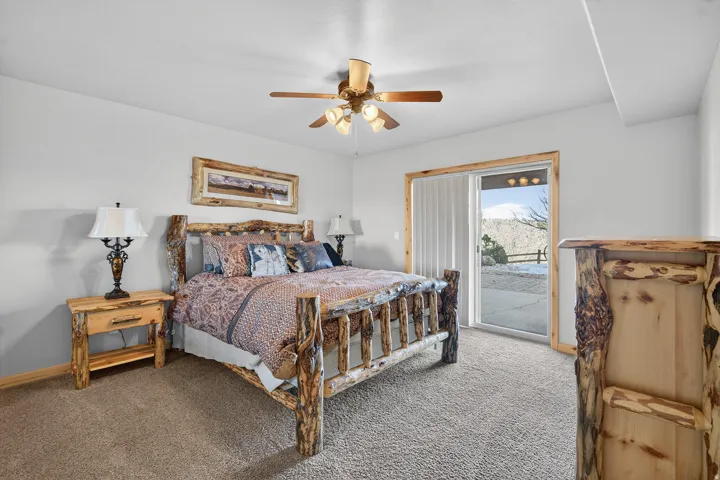 Light gray wall paint, brown carpeting, ceiling fan with integrated lighting, and a sliding glass door leading to an outdoor patio with a concrete surface