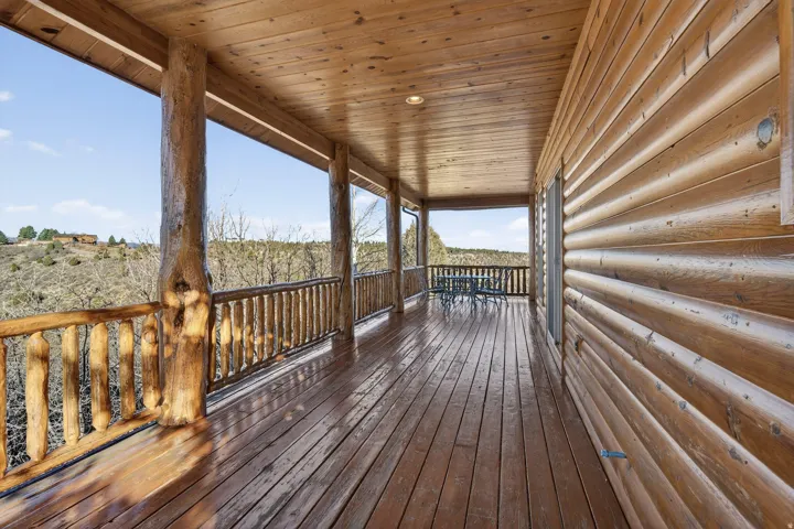 Expansive covered porch featuring wood-finish decking, natural log support columns, log railing, and a matching wood-paneled ceiling