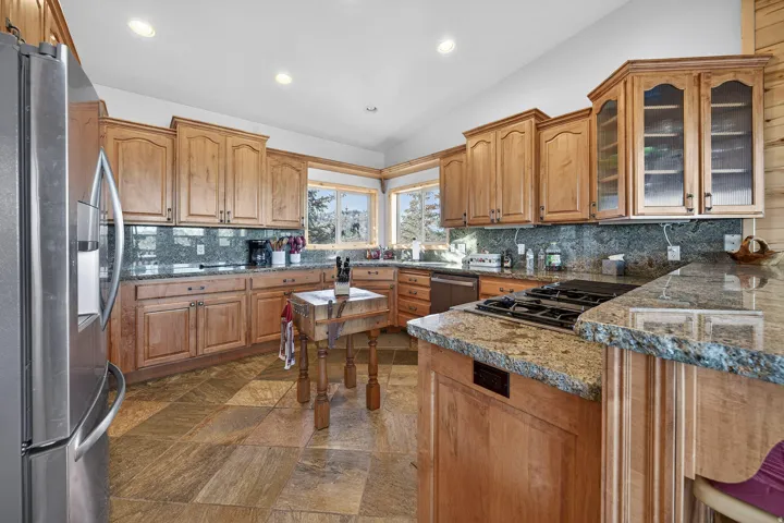 Kitchen featuring light wood cabinetry, granite countertops, a tiled backsplash, stainless steel appliances, and large windows