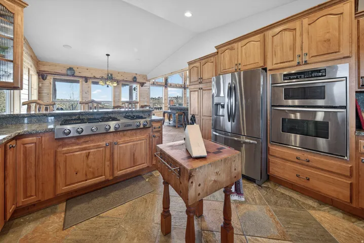 Kitchen featuring wood cabinetry, stainless steel appliances, a built-in range, and stone tile flooring