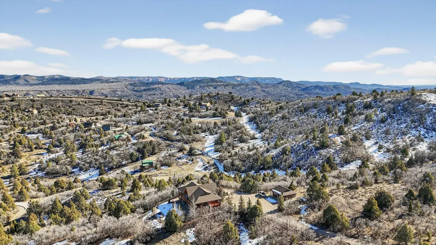 Expansive mountain terrain with scattered evergreen and deciduous trees, featuring a visible residential property with a multi-gabled roof