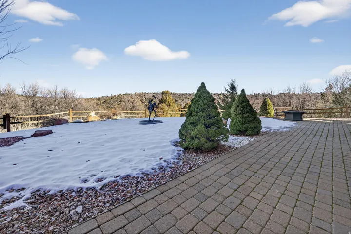 Paver patio with a stone fire pit, bordered by a landscaped area featuring evergreen shrubs and decorative rock