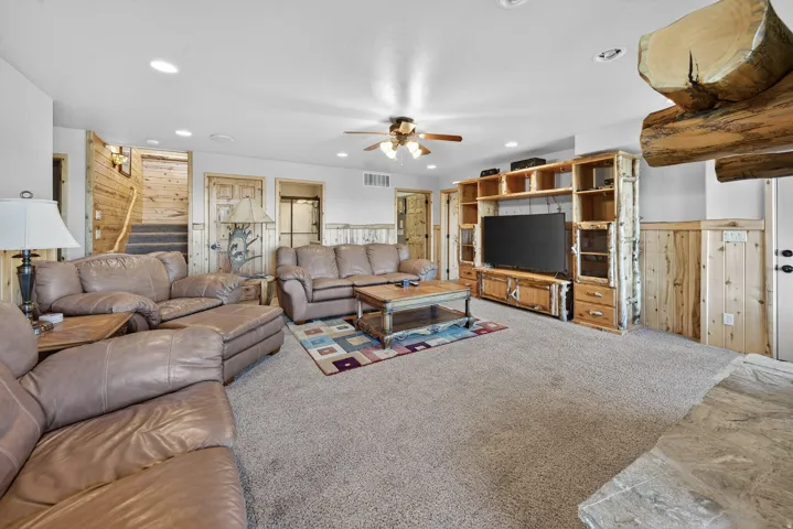 Recessed lighting, ceiling fan, wood-paneled walls, built-in entertainment center, and a carpeted floor