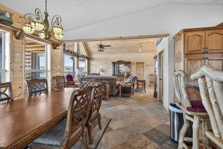 Vaulted ceiling with exposed wood beams, natural wood paneling, tiled flooring, built-in wooden cabinetry, and an ornamental chandelier