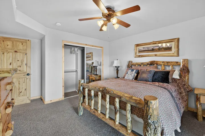 Carpeted flooring, wood-finish ceiling fan with integrated lighting, natural wood door with black hardware, and a closet featuring mirrored sliding doors
