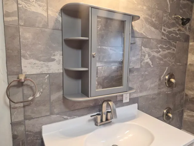 Bathroom featuring large format wall tile, vanity with integrated sink, brushed nickel faucet, and wall-mounted medicine cabinet with integrated shelving