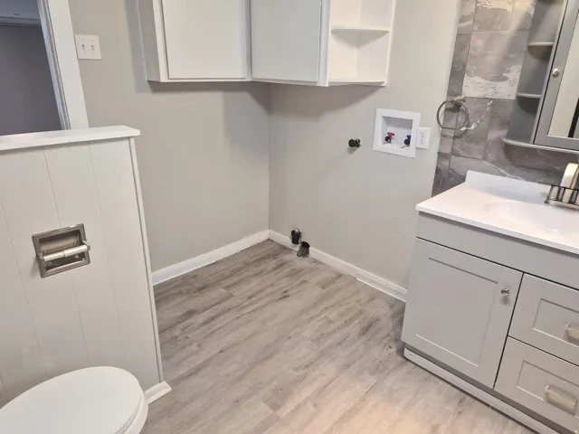Laminate wood-finish flooring, white wall paneling, white built-in cabinetry, gray vanity with white countertop, and gray tiled wall accent
