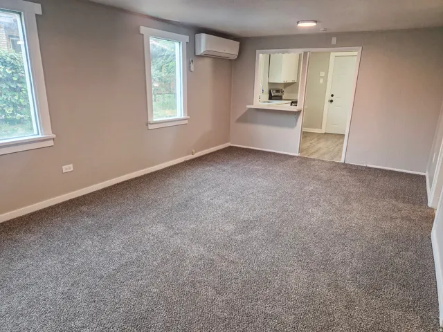Carpeted living area with neutral wall paint, two windows, and a pass-through opening to another room