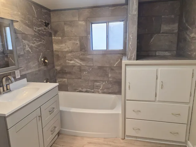 White vanity with an integrated sink and brushed nickel faucet, a soaking tub, and gray tile shower surround