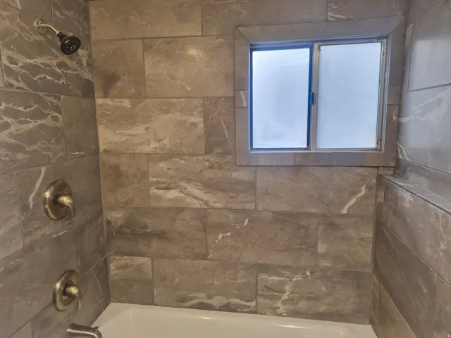 Tub and shower combination featuring tiled walls, an integrated window, a shower head, and bath fixtures