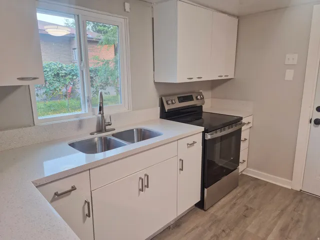 Kitchen featuring white cabinetry, light-toned countertops, a stainless steel double basin sink, and a modern range