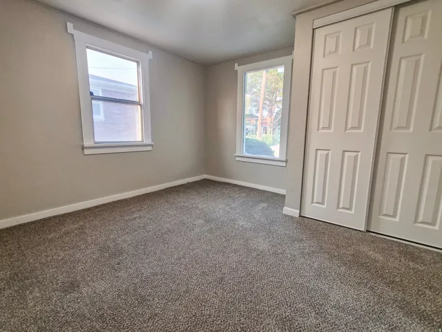 Neutral wall color, two single-hung windows with white trim, and a two-door closet with paneled doors