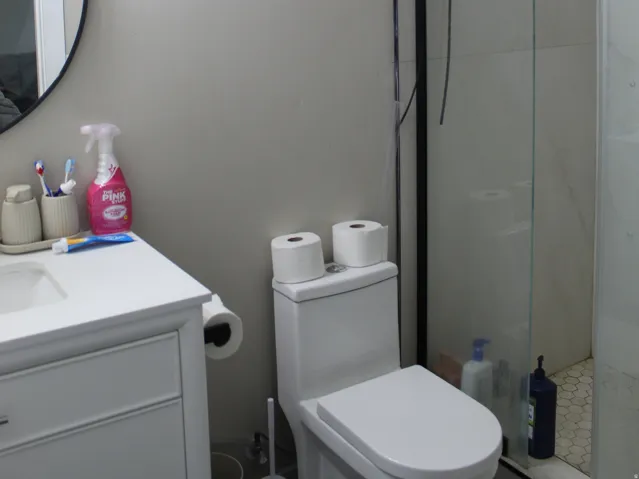 White vanity with a rectangular sink, wall-mounted light fixture, and round mirror