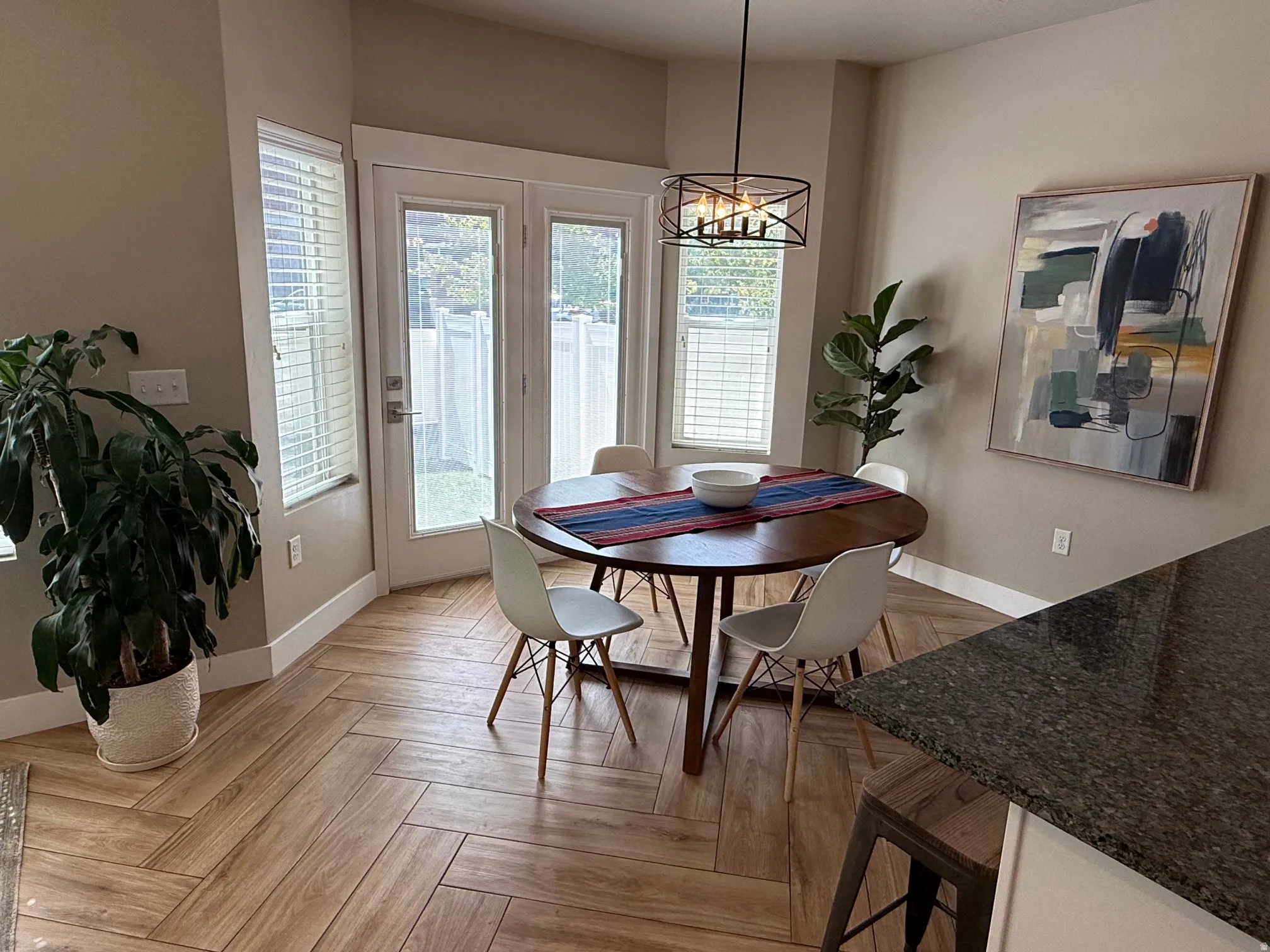 Wood-finish flooring in a herringbone pattern, double glass-paned doors, multiple windows with blinds, and a built-in light fixture