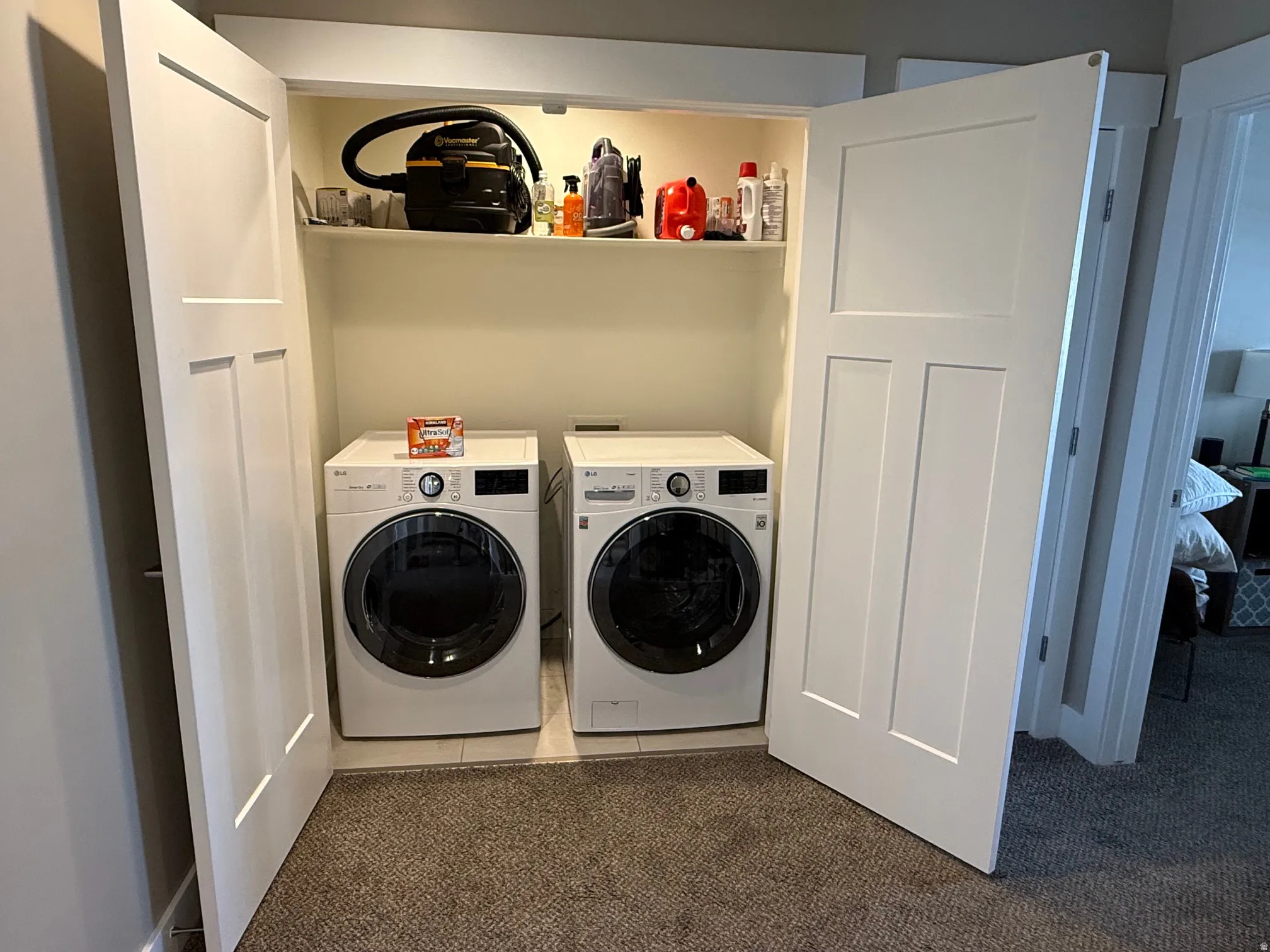 Built-in laundry closet featuring a front-loading washer and dryer, an overhead shelf, and white paneled doors
