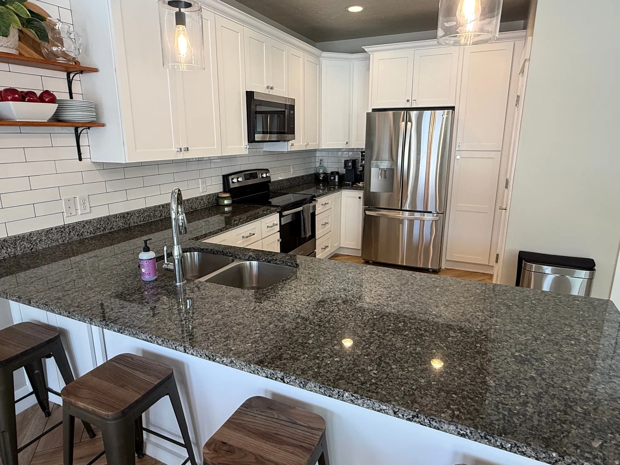 White shaker cabinetry, stainless steel appliances, granite countertops, subway tile backsplash, and recessed and pendant lighting
