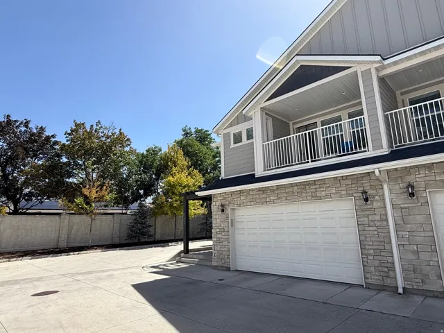 Stone veneer and horizontal siding exterior, attached garage, upper-level balcony with white railing, built-in outdoor lighting, and established perimeter trees