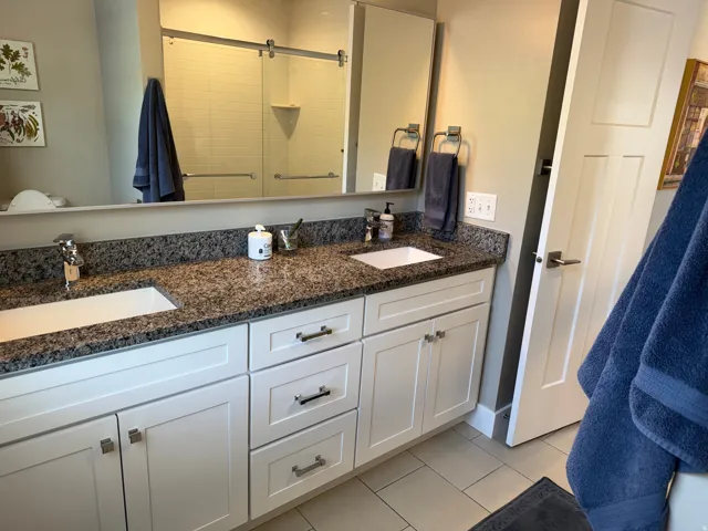 Primary bathroom with Double vanity with white cabinetry, dark speckled countertop, and under-mount sinks