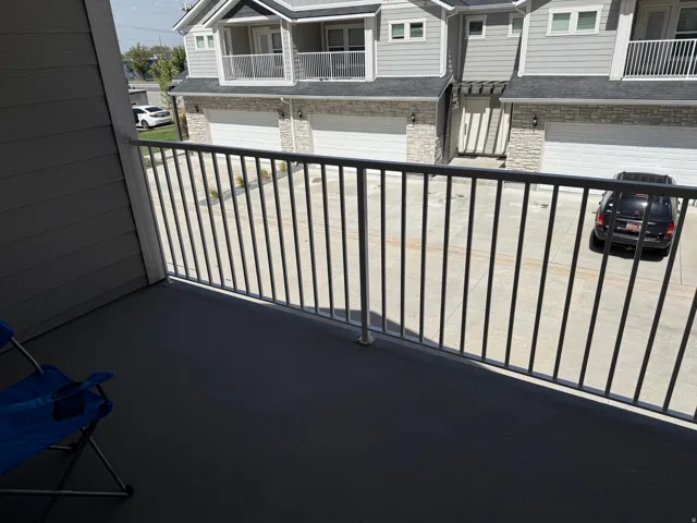 Balcony off primary suite with metal railing overlooking a paved parking area