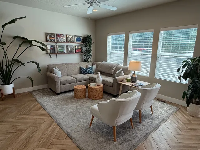 Herringbone wood-finish flooring, multiple windows with blinds, ceiling fan, and wall shelving