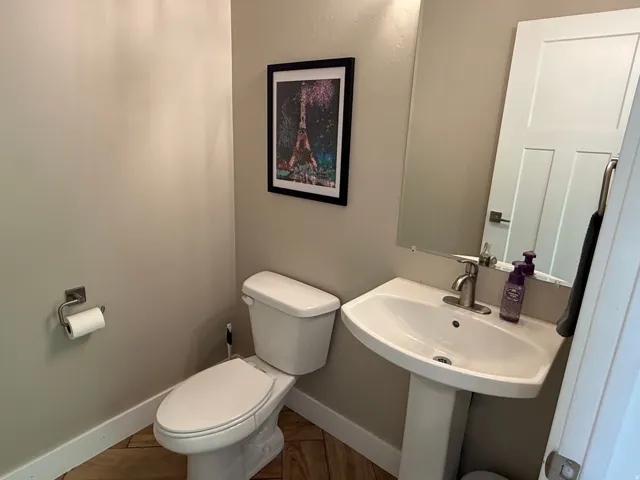 Pedestal sink with a single-handle faucet, white toilet, and wood-finish flooring