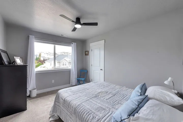 Carpeted room with a large window, a modern ceiling fan with lighting, white trim around the window and door, and neutral gray walls