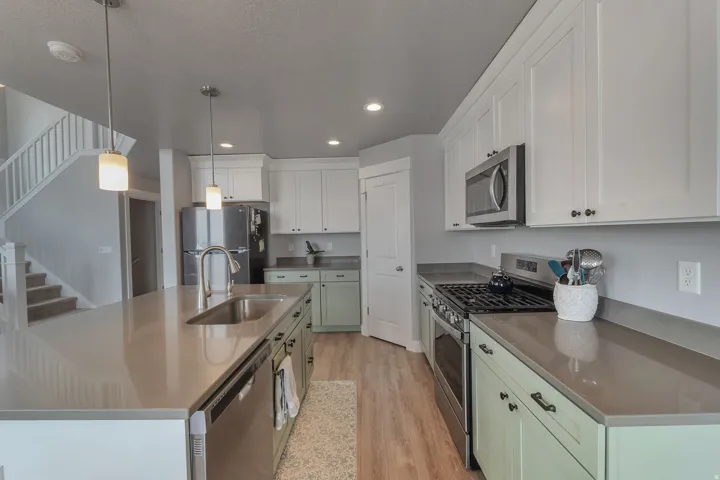 Kitchen featuring white upper cabinetry, light green lower cabinetry, stainless steel appliances, and a large central island with a sink