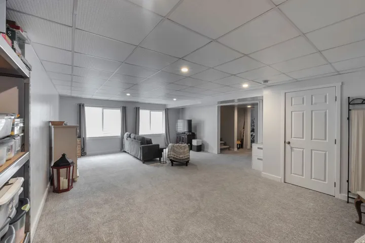 Recessed lighting illuminates the carpeted floor, complemented by multiple windows with neutral drapes