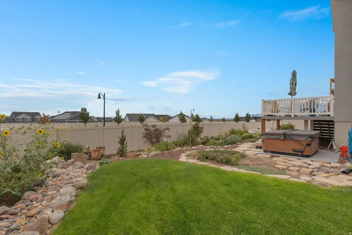 Expansive backyard featuring a manicured lawn, stone pathway, established landscaping, and a hot tub
