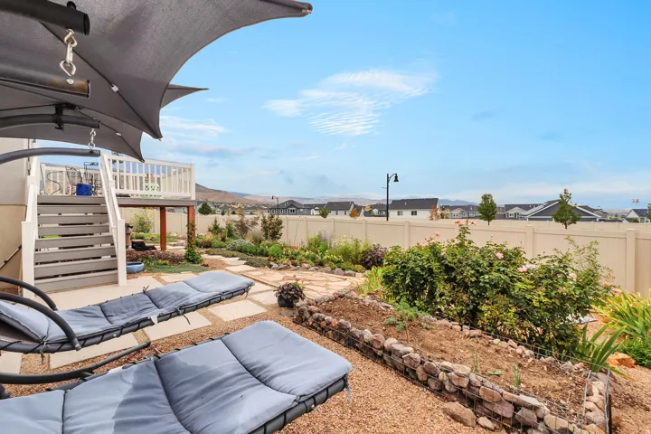 Multi-level outdoor space featuring a covered patio, raised deck with white railings, and a gravel-paved yard with stone-edged garden beds