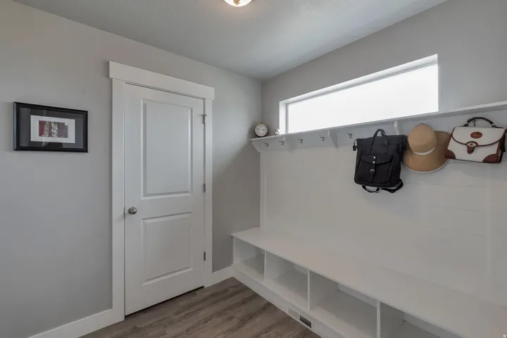Built-in storage bench with individual cubbies and wall hooks, transom window, and wood-finish flooring