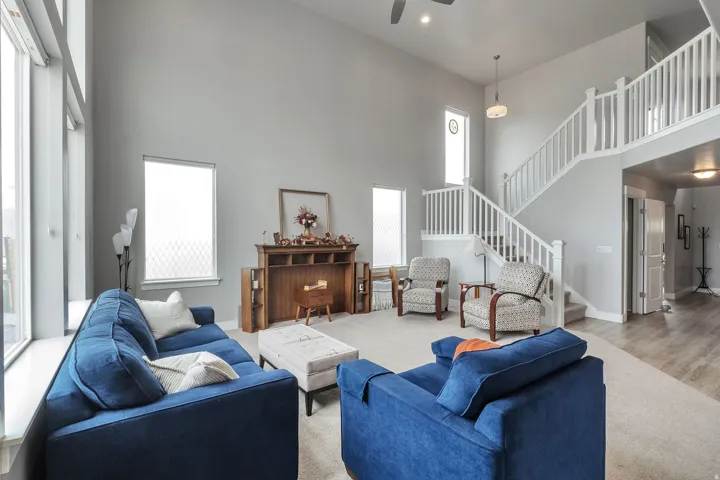 Vaulted ceiling living area with large windows, carpet flooring, a multi-level staircase with white railing, and a loft area
