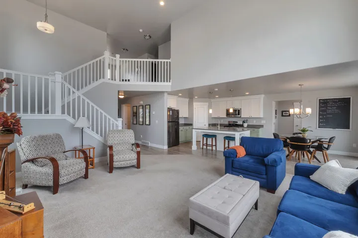 Vaulted ceiling, open-concept design, kitchen island with seating, built-in staircase, and light-toned carpeting