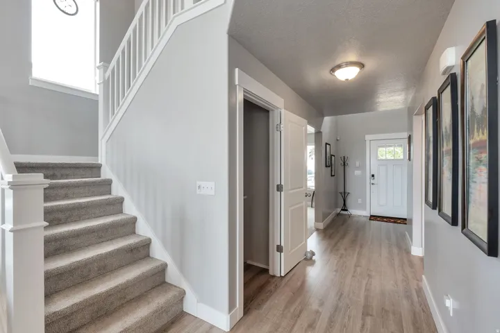Spacious entryway featuring wood-finish flooring, a carpeted staircase with white railings, and a white paneled entry door with decorative glass inserts