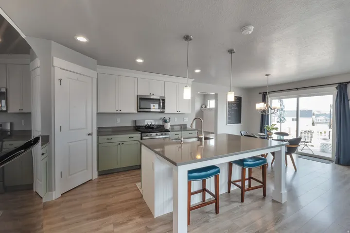 Kitchen featuring a central island with countertop seating, stainless steel appliances, wood-finish flooring, white upper cabinetry, and a glass sliding door