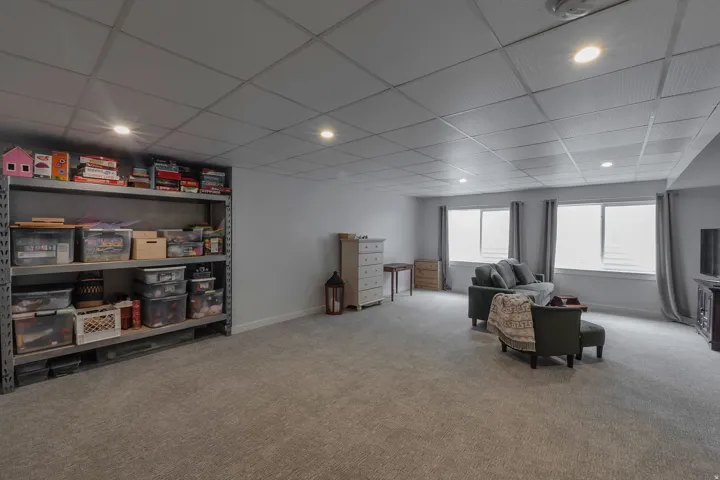 Spacious room featuring light gray carpeting, recessed ceiling lighting, and multiple windows with privacy blinds