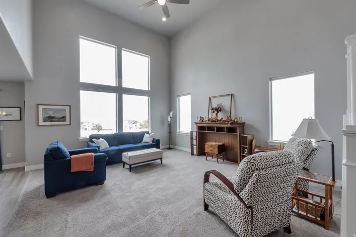 Vaulted ceiling, ceiling fan, large multi-pane windows, light gray wall color, light gray carpet flooring