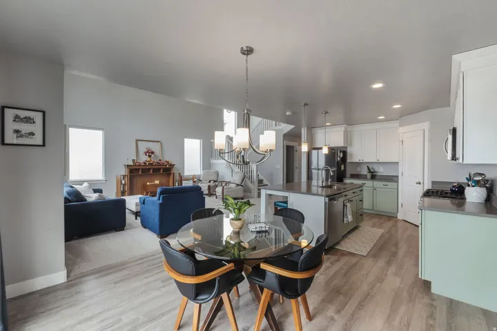 Open-concept living space featuring wood-finish flooring, a kitchen island, stainless steel appliances, white and light green cabinetry, and a staircase with a wrought-iron railing
